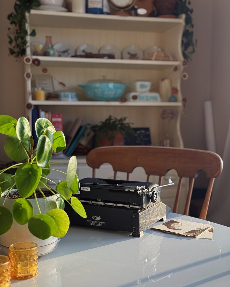 A vintage Royal typewriter on a table in front of a styled shelf with dishes and plants