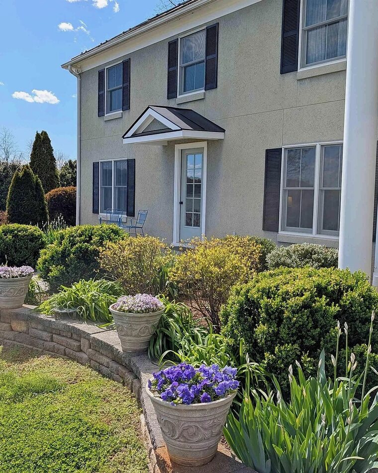 Front entrance of the farmhouse with a stone planter wall and flowering plants