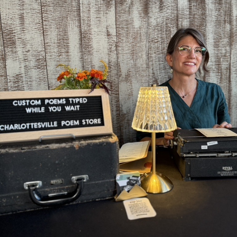 Laura Frantz at a Charlottesville Poem Store setup with a custom-poems sign